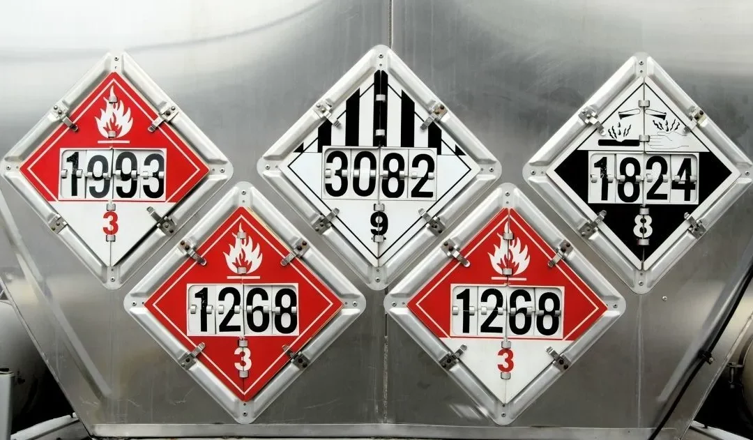 Hazmat warning decals on a tank of hazardous materials being hauled by a semi-truck.