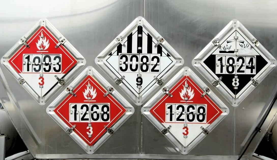 Hazmat warning decals on a tank of hazardous materials being hauled by a semi-truck.
