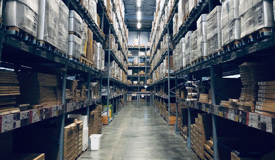 A warehouse aisle holds packages that are stacked on shelves from floor to ceiling.