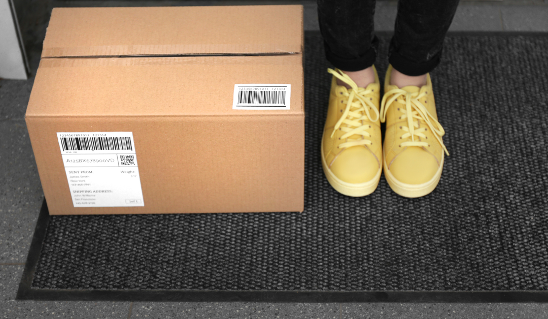 A discreetly packaged shipping box placed on a doorstep, with a customer's shoes visible beside it.