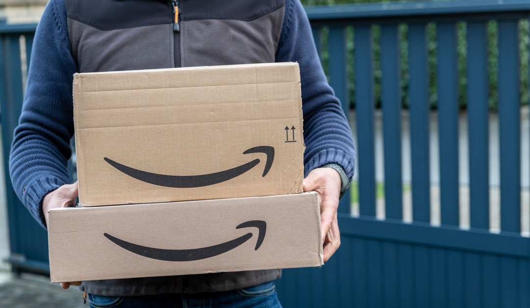 A person, whose torso is showing only, is holding two amazon boxes.