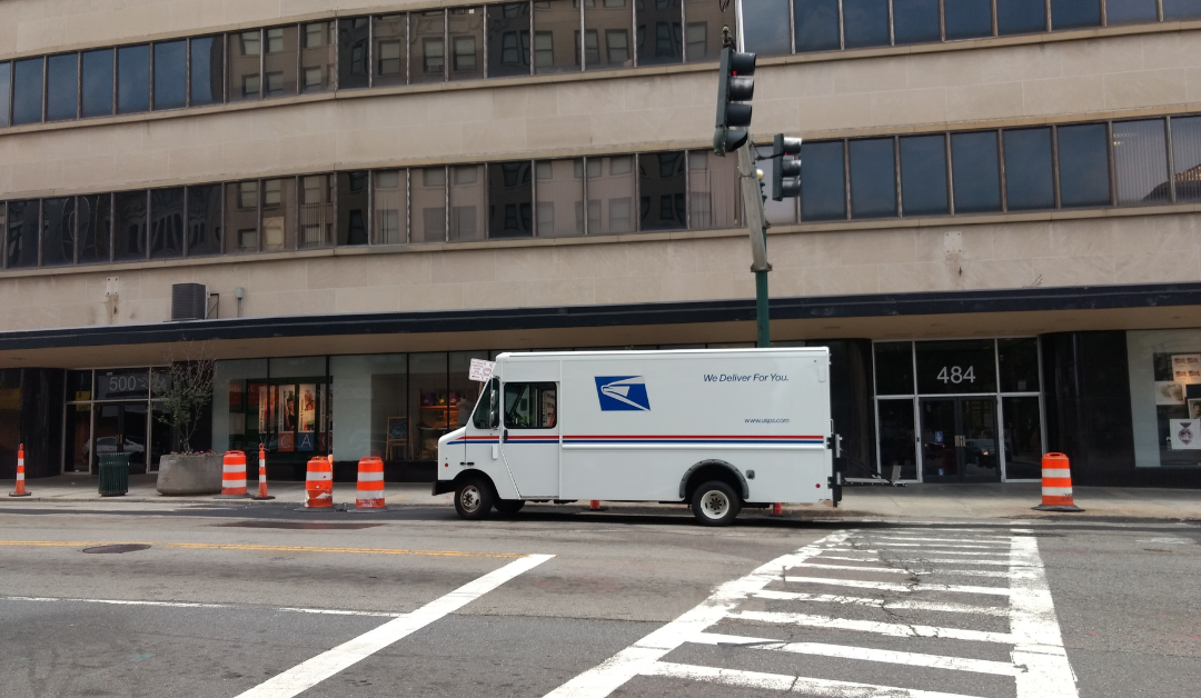 A white USPS mail truck parked on the curb of an empty city street