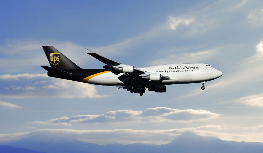 A UPS plane flies in a cloudy sky, signifying the speedy delivery to be gained when using 2nd Day Air UPS services.