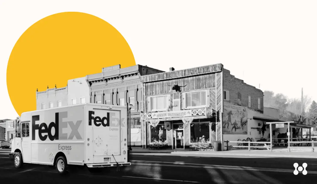 A FedEx truck is shown in the foreground in black and white. Behind the truck is a street with low, old buildings. A stylized yellow sun rises in the background. 